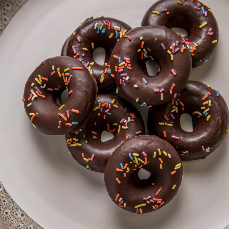 A close-up view of chocolate donuts with colorful sprinkles on a white plate, ready to be enjoyed.