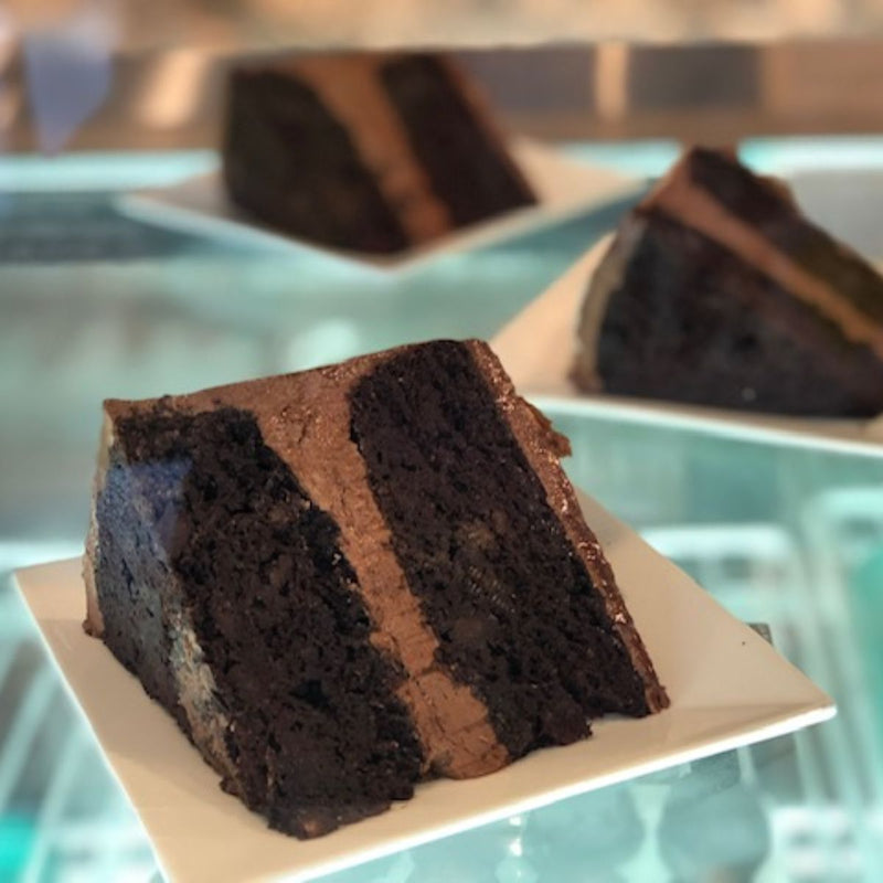 Slices of chocolate cake with chocolate frosting on white plates.