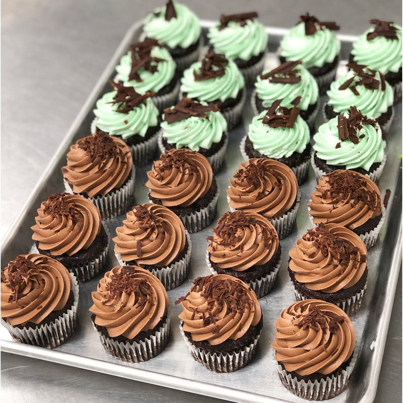 A tray of chocolate cupcakes, half with mint green frosting and chocolate shavings, half with chocolate frosting.