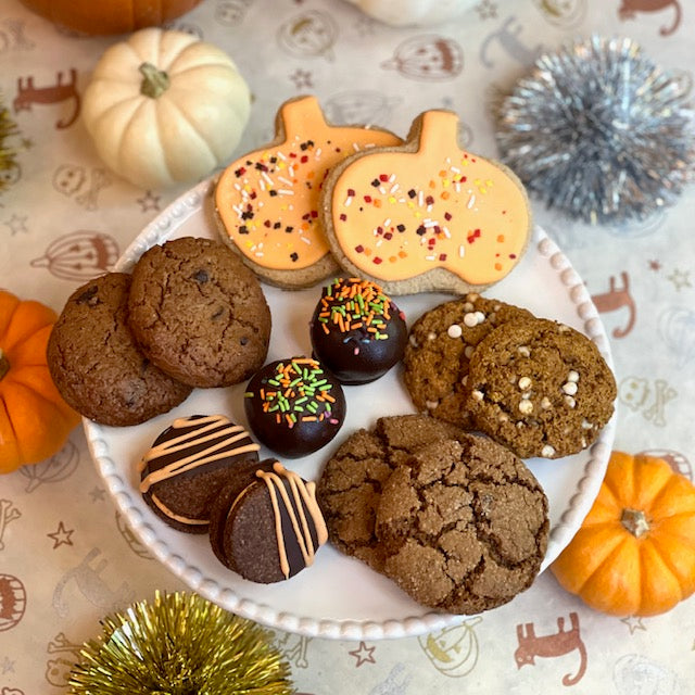 A white plate with various Halloween-themed cookies and chocolates on a festive tablecloth.