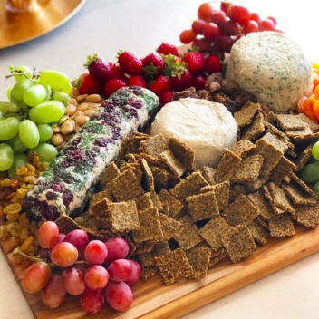 A large wooden charcuterie board filled with grapes, strawberries, nuts, cheese, and crackers.