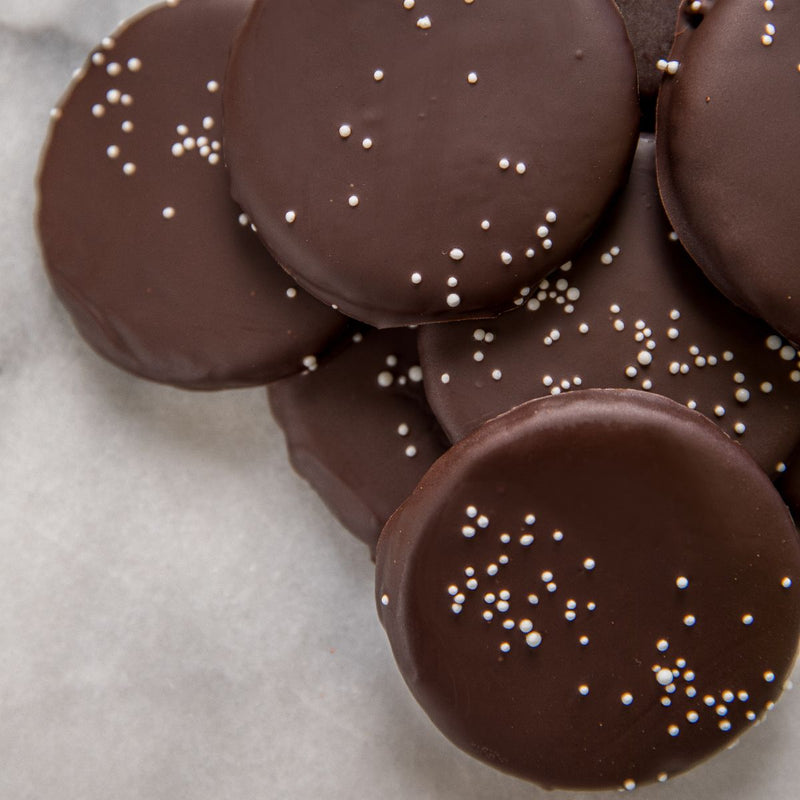 A close-up of several dark chocolate-covered peppermint patties with white sprinkles.