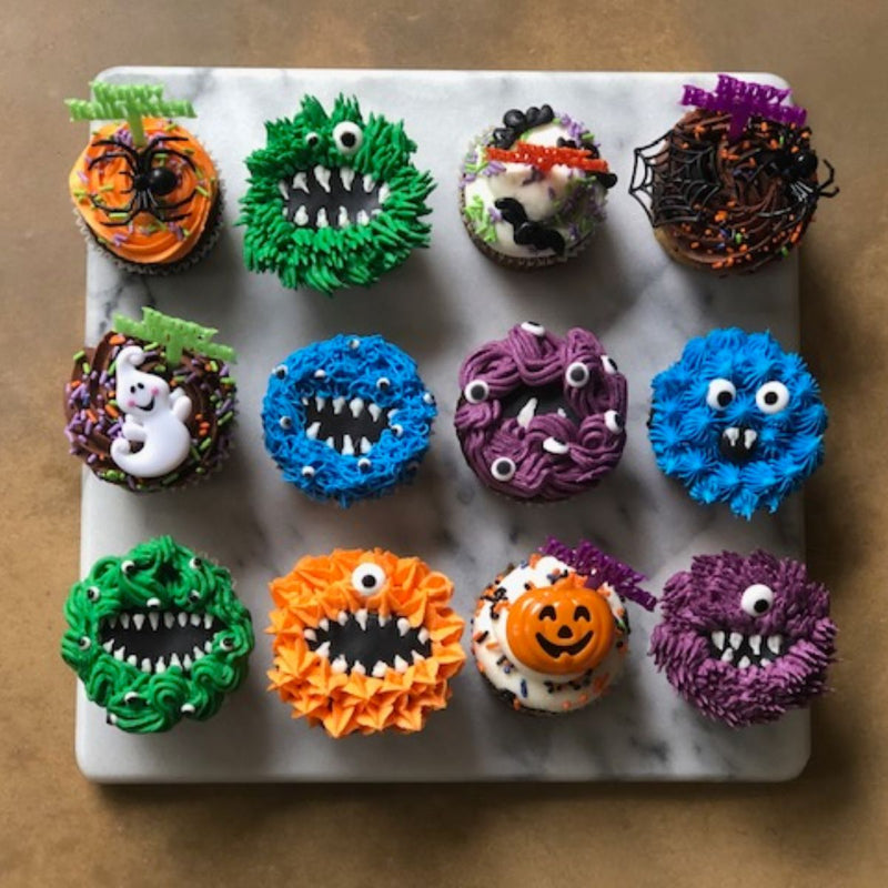 Twelve Halloween cupcakes decorated as monsters, a ghost, a pumpkin, and spiders on a web.