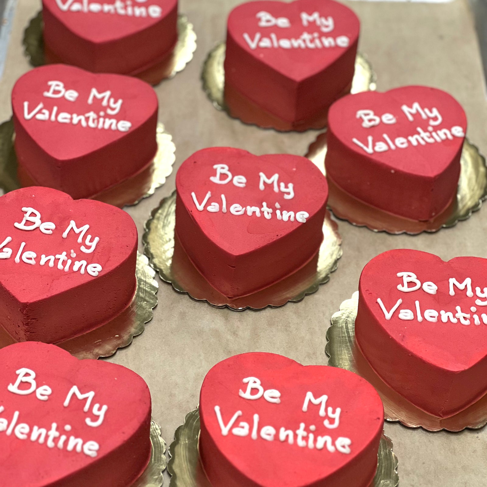 Nine heart-shaped Be My Valentine Cakes with red frosting.