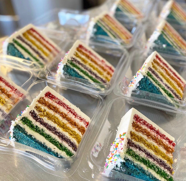 Multiple slices of rainbow-layered Pride Cake in clear containers.