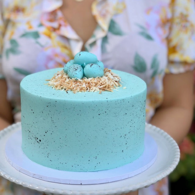 Easter Speckled Blue Egg Nest Cake held by a person in a floral shirt.